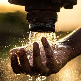 Hand being held under water flowing from an industrial pipe.