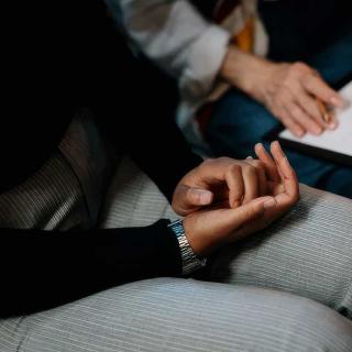 Two individuals sit together looking at a tablet screen, one with hands held in a worried fashion.