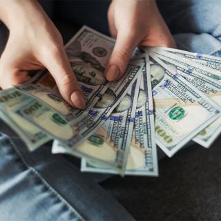 Woman's hands holding a fanned out stack of $100 bills.