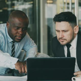 Two men in suits, reviewing something on a computer.