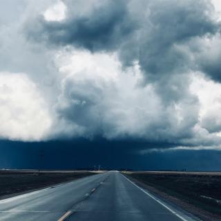 Dramatic highway scene with large dark storm clouds building over the road ahead.