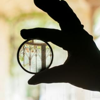 Gloved hand holding a magnifying lens in front of a blurry background, bringing it into focus
