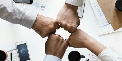 Four business people with their fists touching over a messy white desk