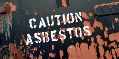 Photo of a destressed wall with the words 'CAUTION ASBESTOS' painted on it